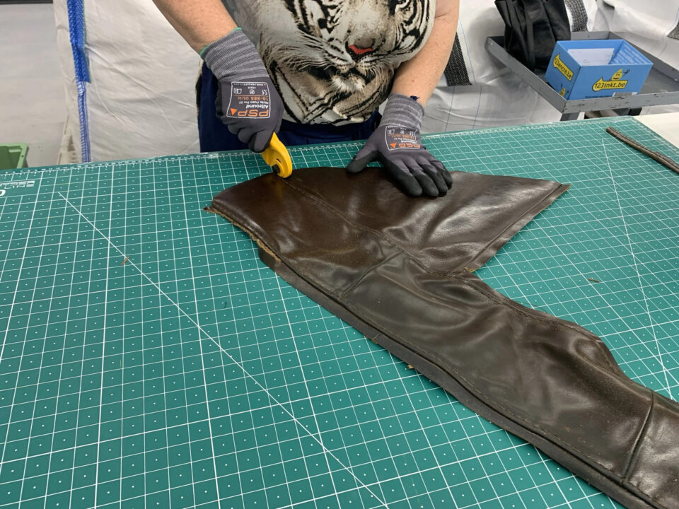 Gloved hands cutting a dark brown leather piece on a green cutting mat