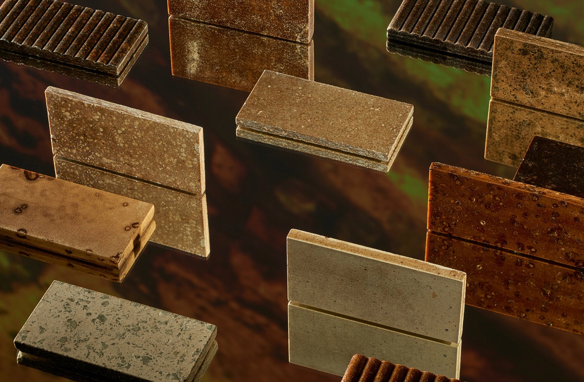 Rectangular biocomposite tiles in amber and stone tones floating against a dark background