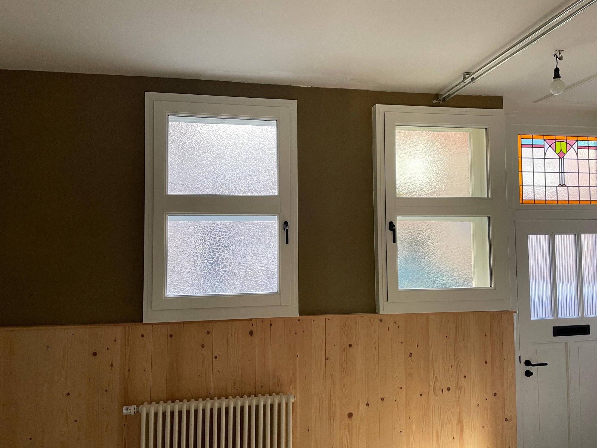Room with an olive green BioStuc wall, white windows and pine wood panelling