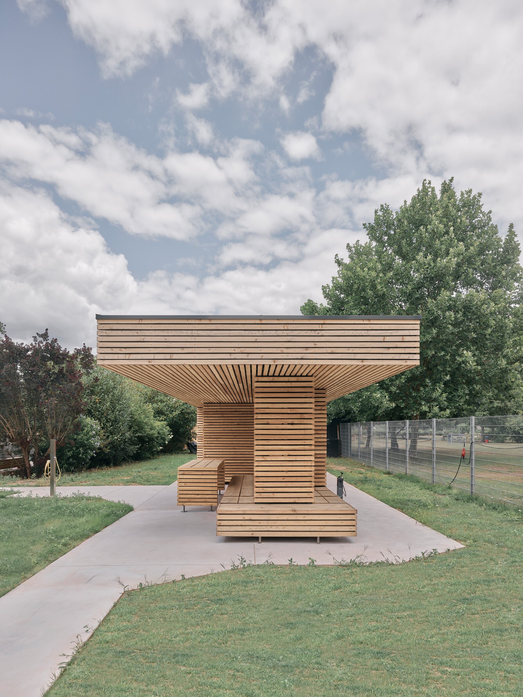 Compact timber building clad in horizontal larch boards with a wide overhanging roof on a lawn
