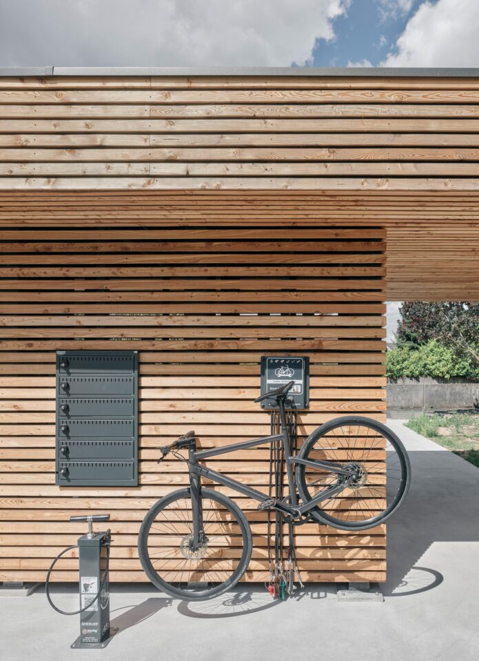 Bicycle parked against a larch-clad wall with a charging point and repair stand