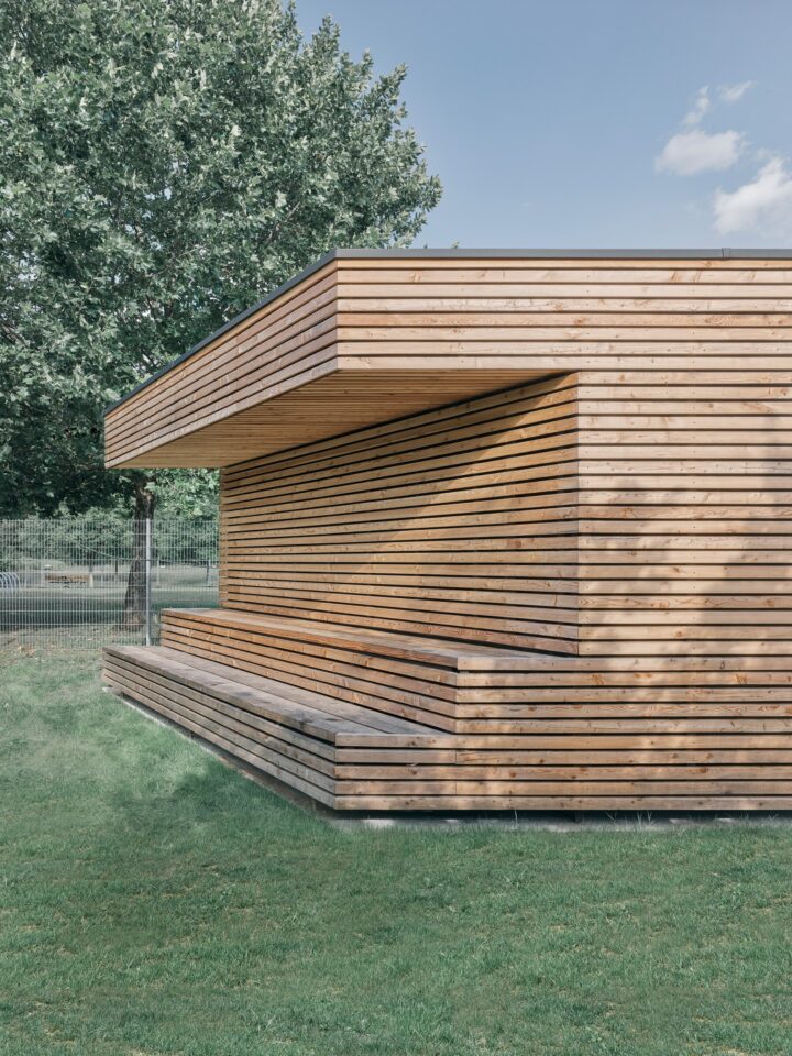 Corner of a larch-clad building with a recessed bench and deep overhang