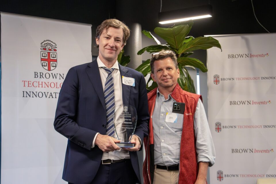 Derek Stein holding a glass award next to Greg Hirth in front of a Brown Technology Innovations backdrop