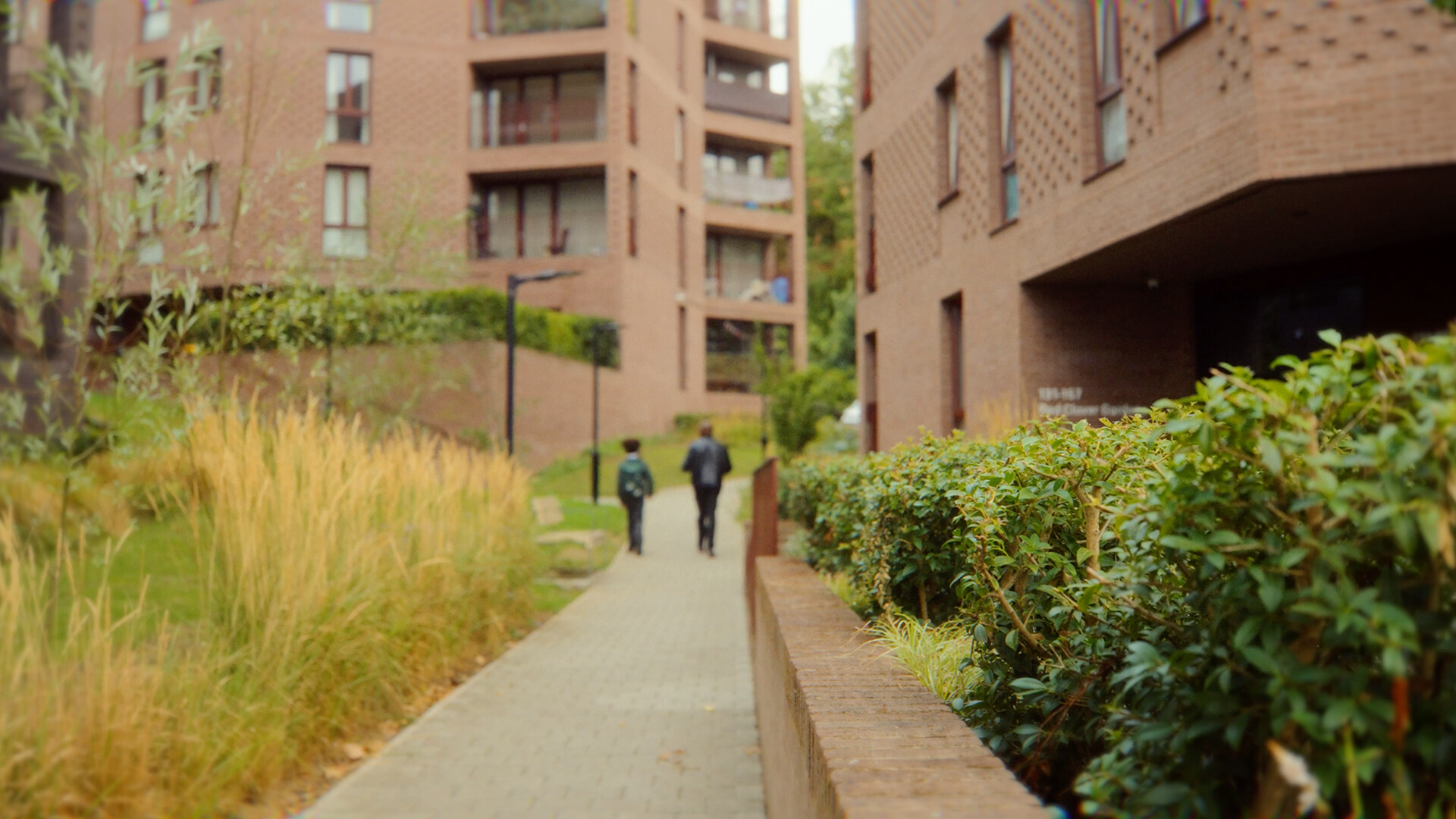 Two people walking on a path between brick housing blocks and planted borders