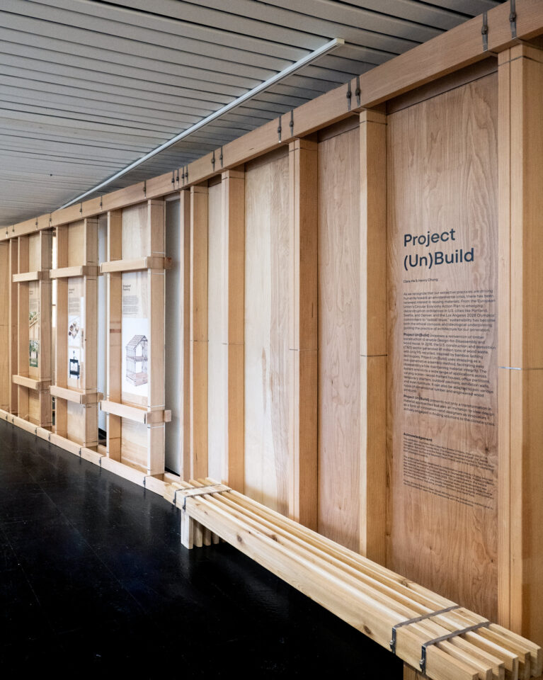 Exhibition wall of timber framing and plywood with a strapped bench in front