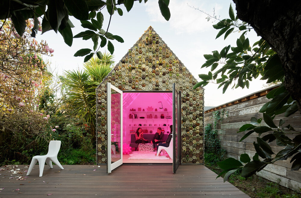 Backyard cabin clad in 3D printed ceramic tiles with an illuminated pink interior